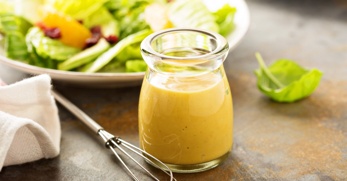 barattolino pieno di dressing a base di kombucha, con insalata sullo sfondo
