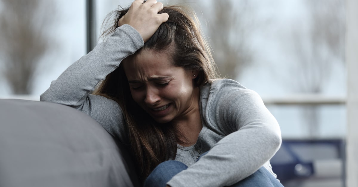 Donna sul divano di casa che piange sconsolata