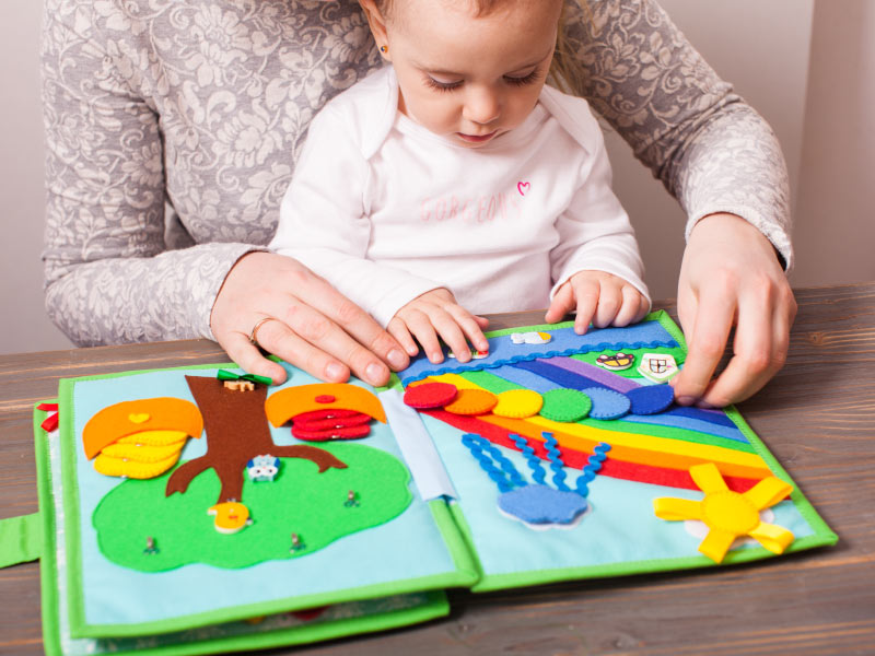 Mamma che sfoglia insieme alla sua bimba un libro tattile di stoffa