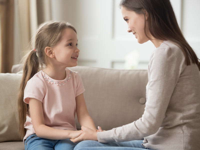 Una mamma parla con la sua bambina tenendole le mani e guardandola negli occhi