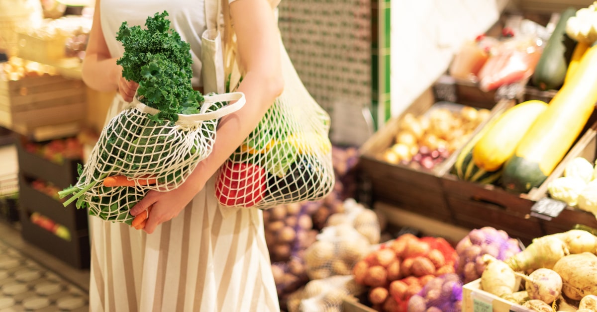 Donna che compra verdura sfusa con borse in cotone riutilizzabili 