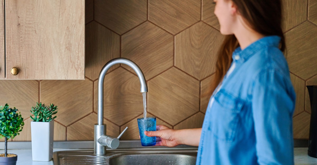 Donna che prende un bicchiere di acqua dal rubinetto della cucina