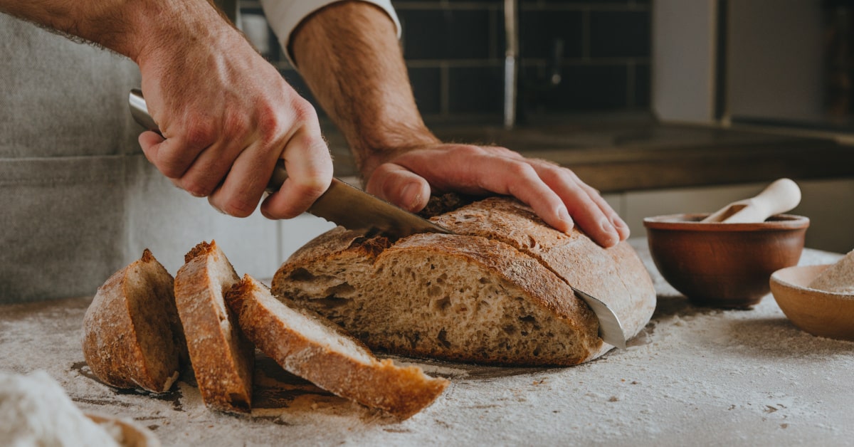 Uomo che taglia il pane con il coltello: il pane è un alimento processato