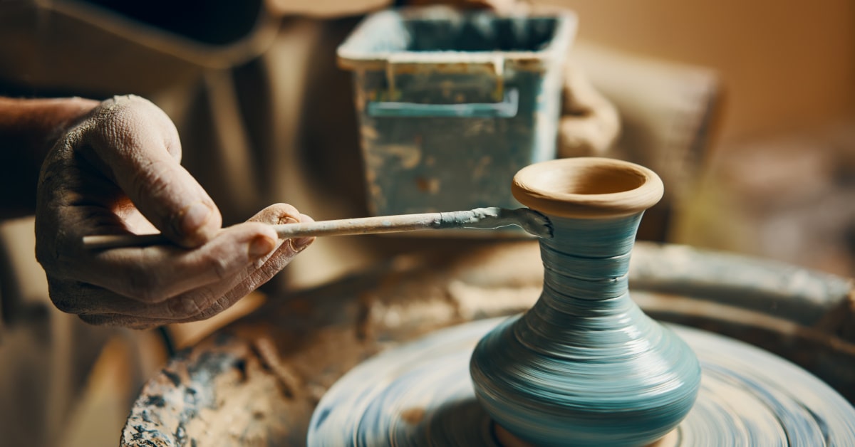 Mani maschili che colorano una brocca di ceramica sul tornic