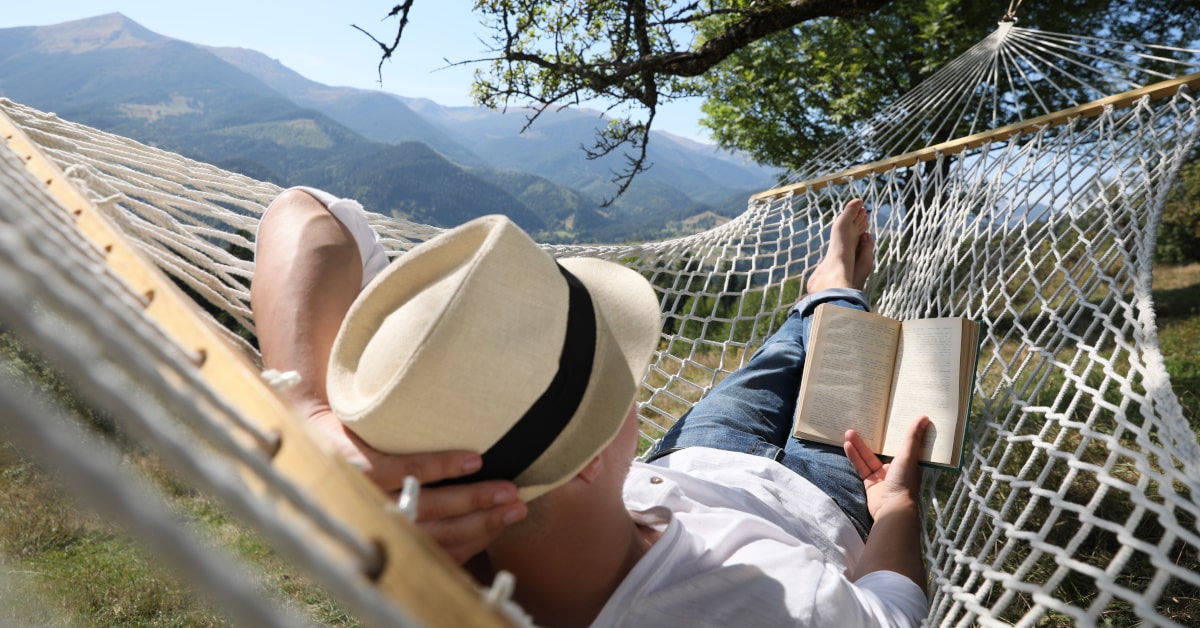 Giovane uomo steso su un'amaca mentre legge un libro
