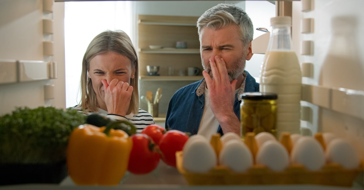 Marito e moglie davanti al frigo aperto con cattivo odore per cibo andato a male e spreco alimentare