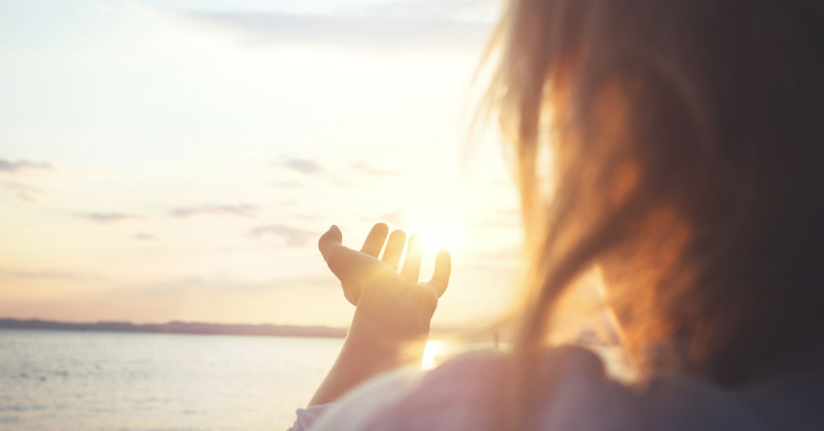 Donna all'aperto che allunga una mano verso il sole