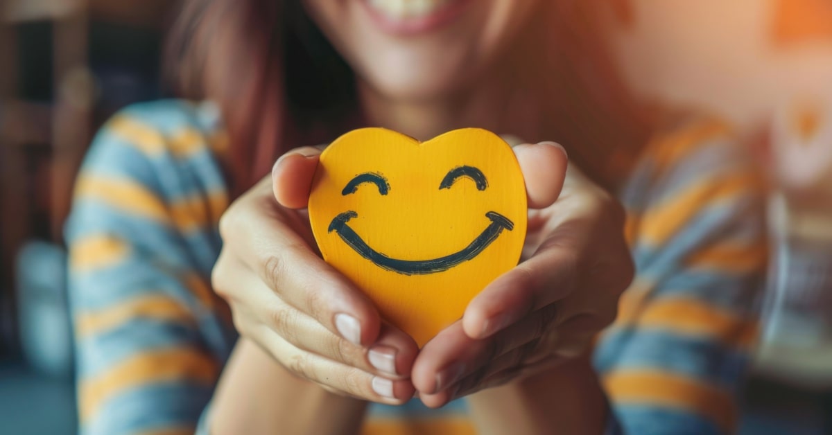 Donna che tiene un cuore giallo sorridente di legno fra le mani