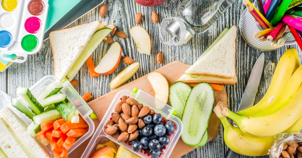 Tavolo con colori, penne e quaderni e spuntini sani a base di frutta e verdura