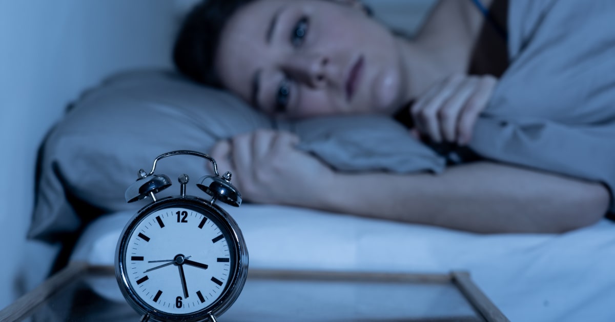 Donna stesa a letto sveglia nel cuore della notte con sveglia sul comodino che segna le 3.30