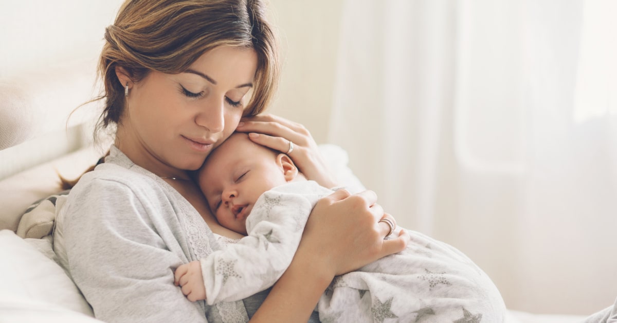 Mamma seduta sul divano che abbraccia il proprio neonato mentre dorme