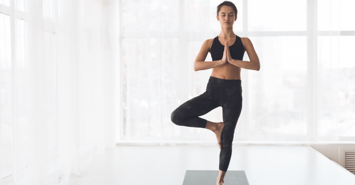Donna in casa che pratica yoga nella posizione dell'albero