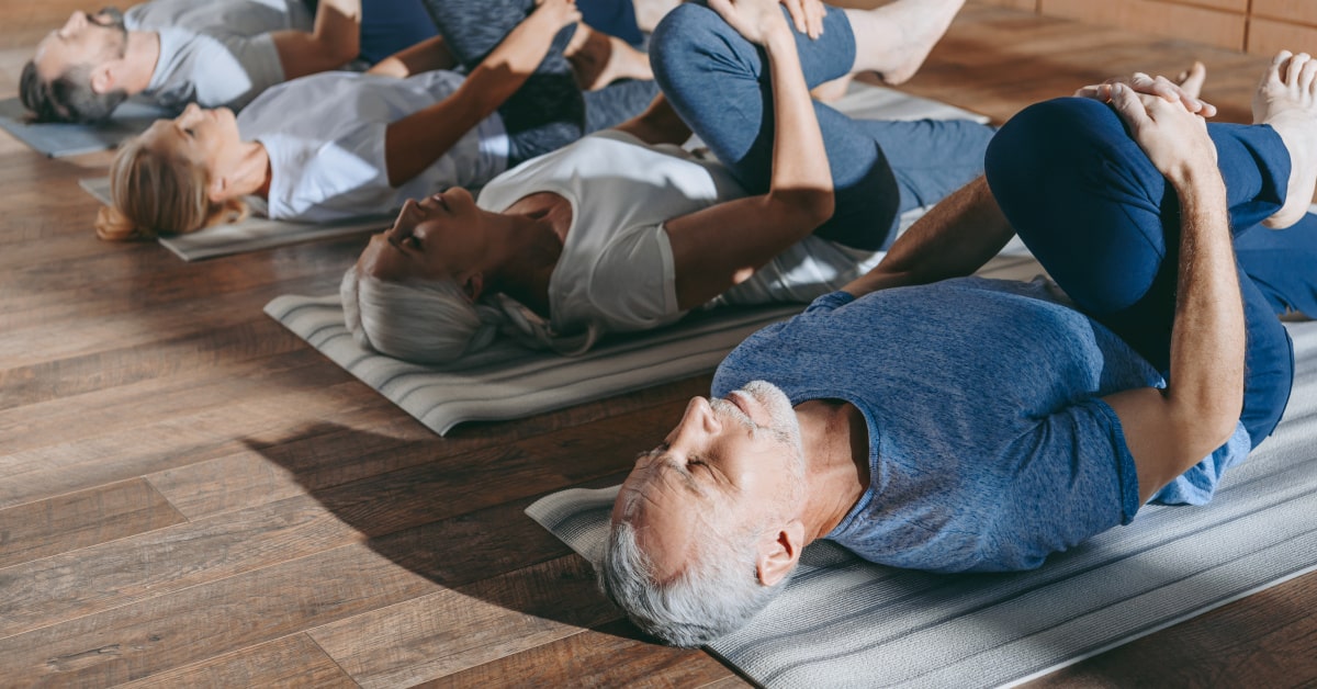 Gruppo di persone mature che fa stretching sul tappetino da yoga