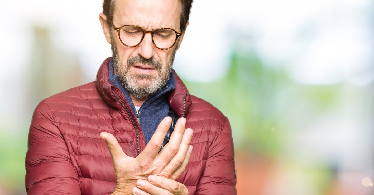 Uomo con giacca invernale con dolore alla mano