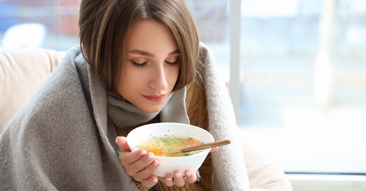 Donna malata con coperta sulle spalle con piatto di brodo caldo di verdure fra le mani