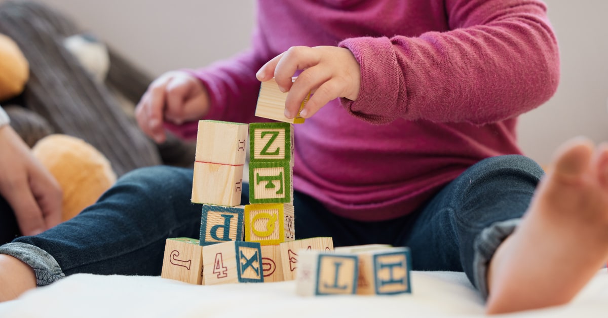 Bambina che gioca su materasso colorato con blocchi con lettere e numeri