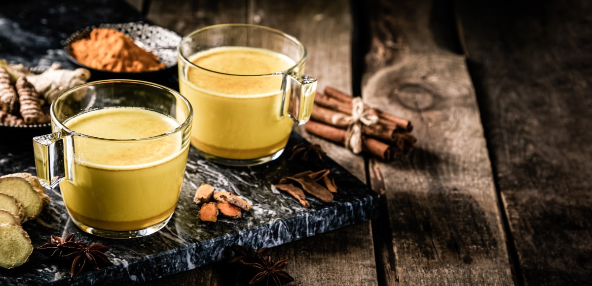 Due tazze di golden milk su vassoio nero e tavolo in legno