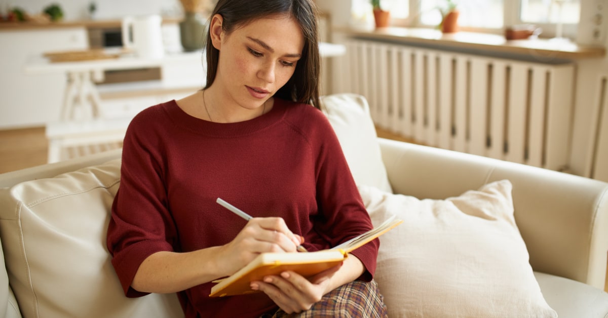 Donna seduta sul divano mentre scrive su un quaderno