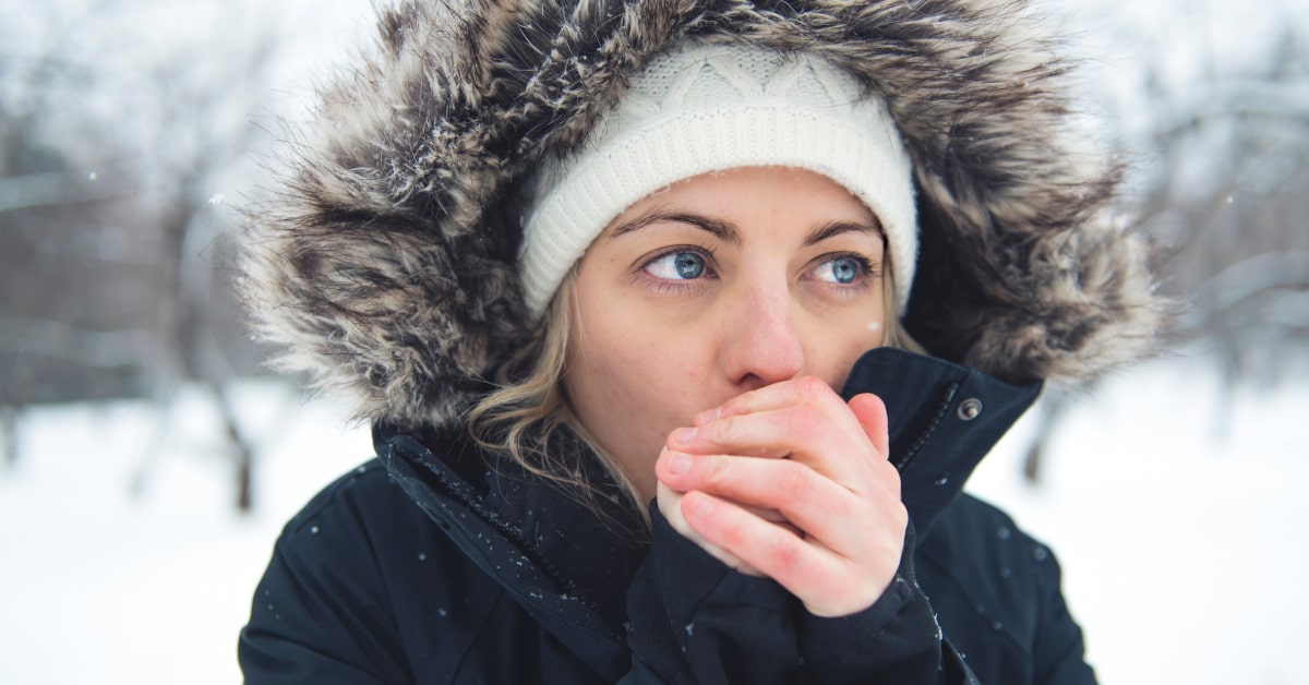 Donna all'aperto in inverno che si scalda le mani con il respiro