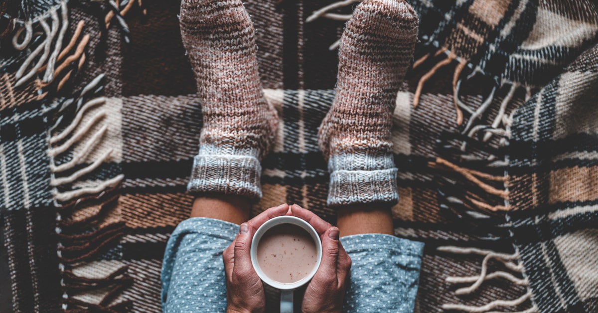 piedi di donna in calzettoni di lana e seduta su una coperta mentre tiene fra le mani una bevanda calda
