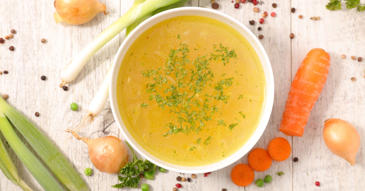 Ciotola con brodo vegetale e verdure crude sul tavolo