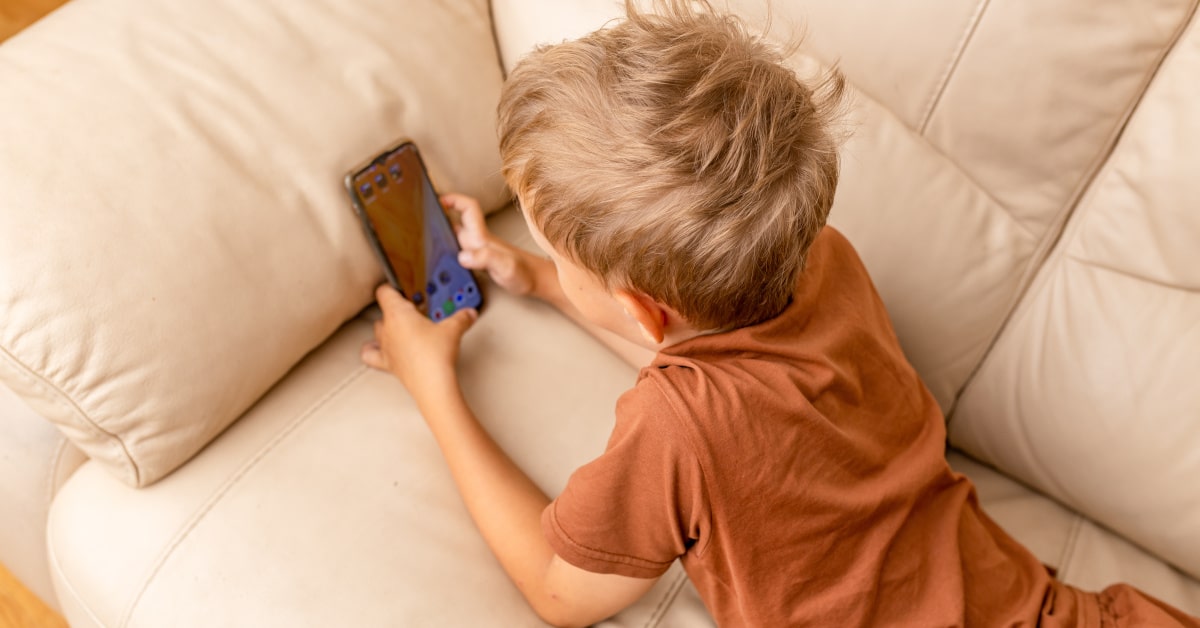 Bambino steso sul divano mentre guarda uno smartphone