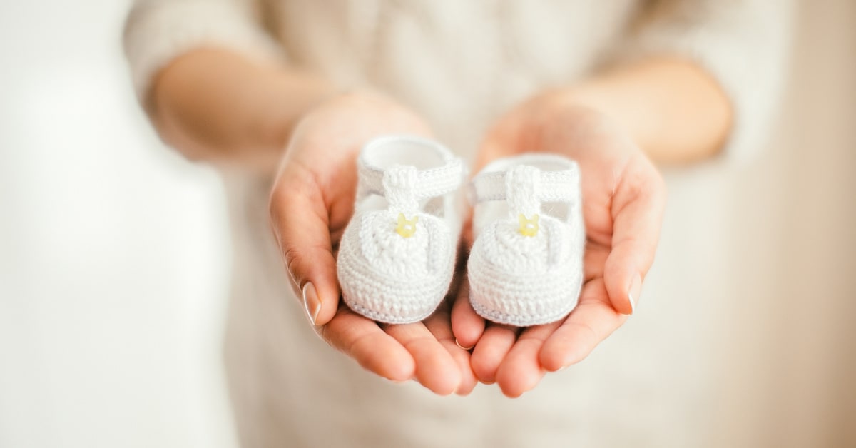 Donna incinta che tiene in mano delle scarpine da neonato