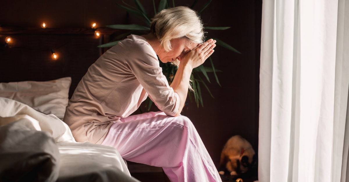 Donna di mezza età triste, seduta al bordo del letto