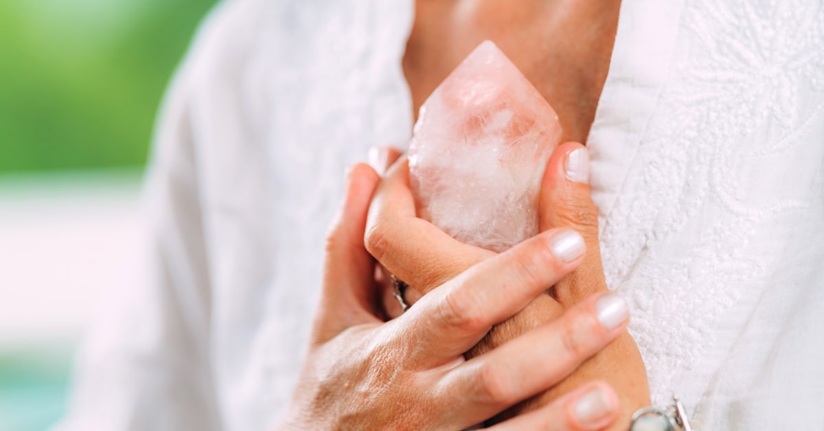 Donna che tiene fra le mani un cristallo di quarzo rosa all'altezza del cuore