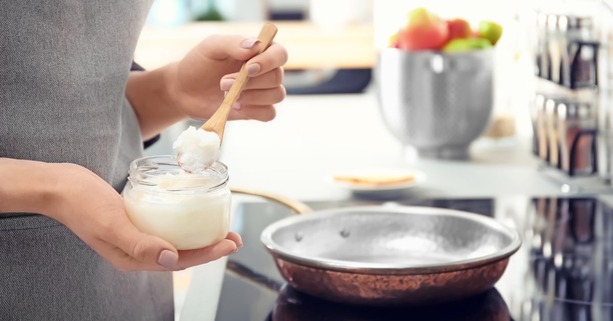 Donna ai fornelli che aggiunge un cucchiaino di olio di cocco in una padella