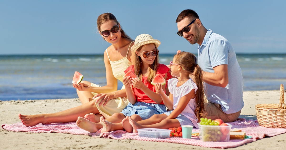 Famiglia con bambini mentre mangia frutta di stagione in spiaggia