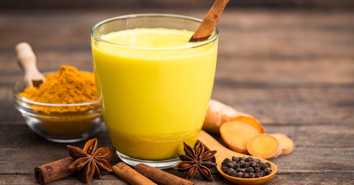 Bicchiere con golden milk, la bevanda dorata, e spezie sul tavolo