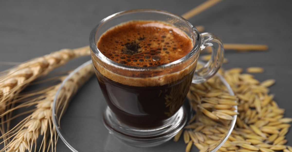 Tazzina in vetro con caffè d'orzo e chicchi di orzo sparsi sul tavolo