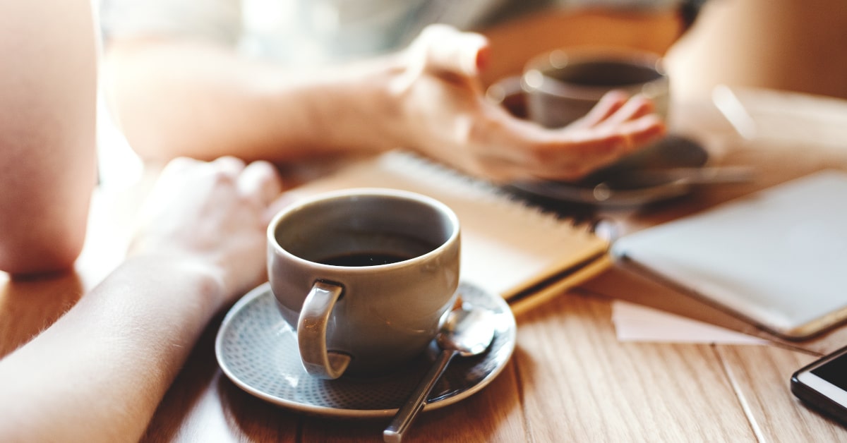 Due tazzine di caffè in primo piano con due amici che parlano 