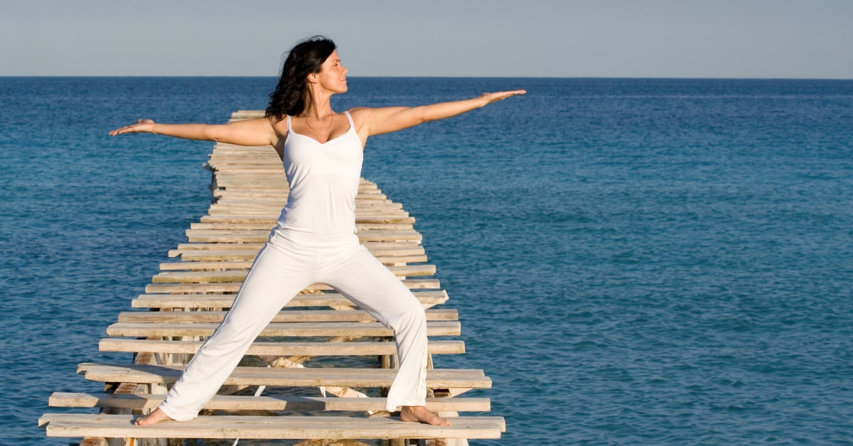 Donna vestita di bianco che fa tai chi sul pontile di un lago