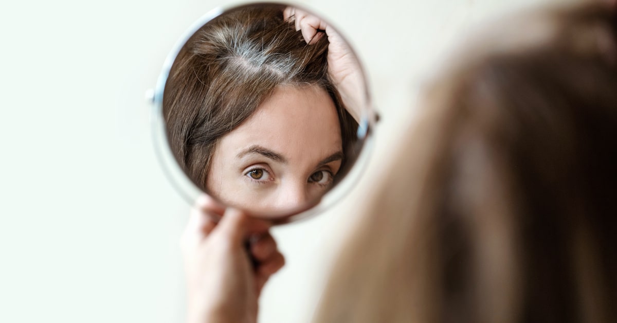 Donna che osserva i capelli bianchi in uno specchio