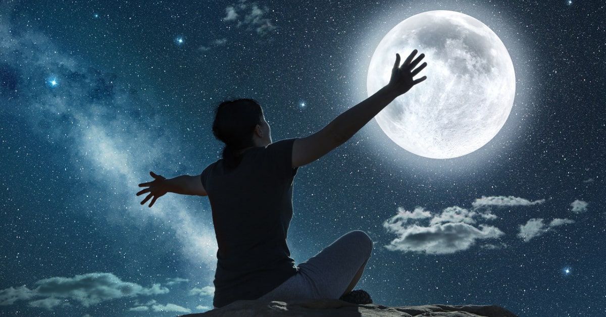 Donna seduta su una roccia con le braccia aperte rivolta alla luna piena