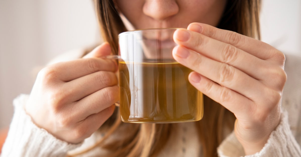 Primo piano di donna che beve una tisana da una tazza di vetro trasparente