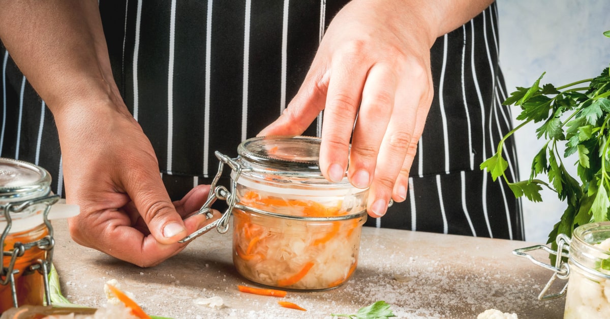 Uomo in cucina che chiude un vasetto di vetro con verdure fermentate