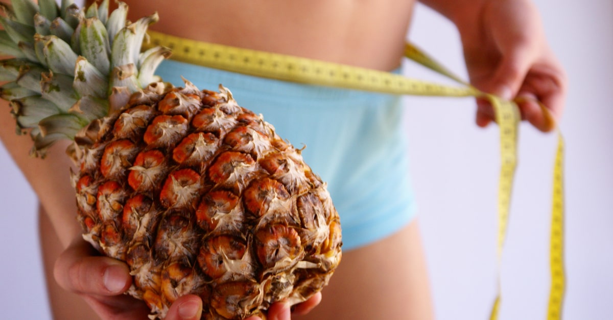 Donna che misura la circonferenza della vita con un metro e un'ananas in mano