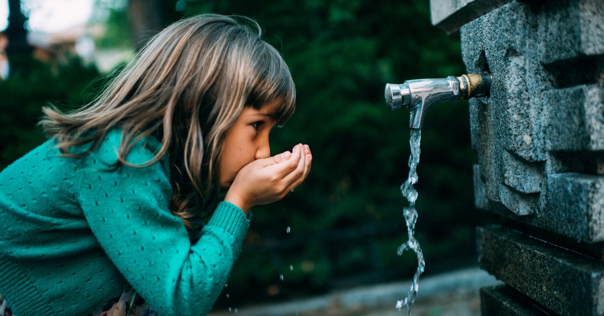 Bambina beve acqua da una fontana pubblica