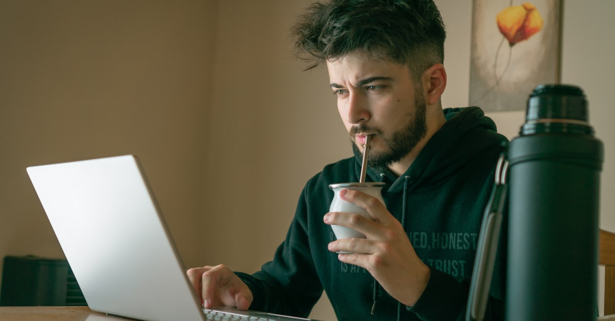 Giovane uomo davanti al PC mentre beve yerba mate