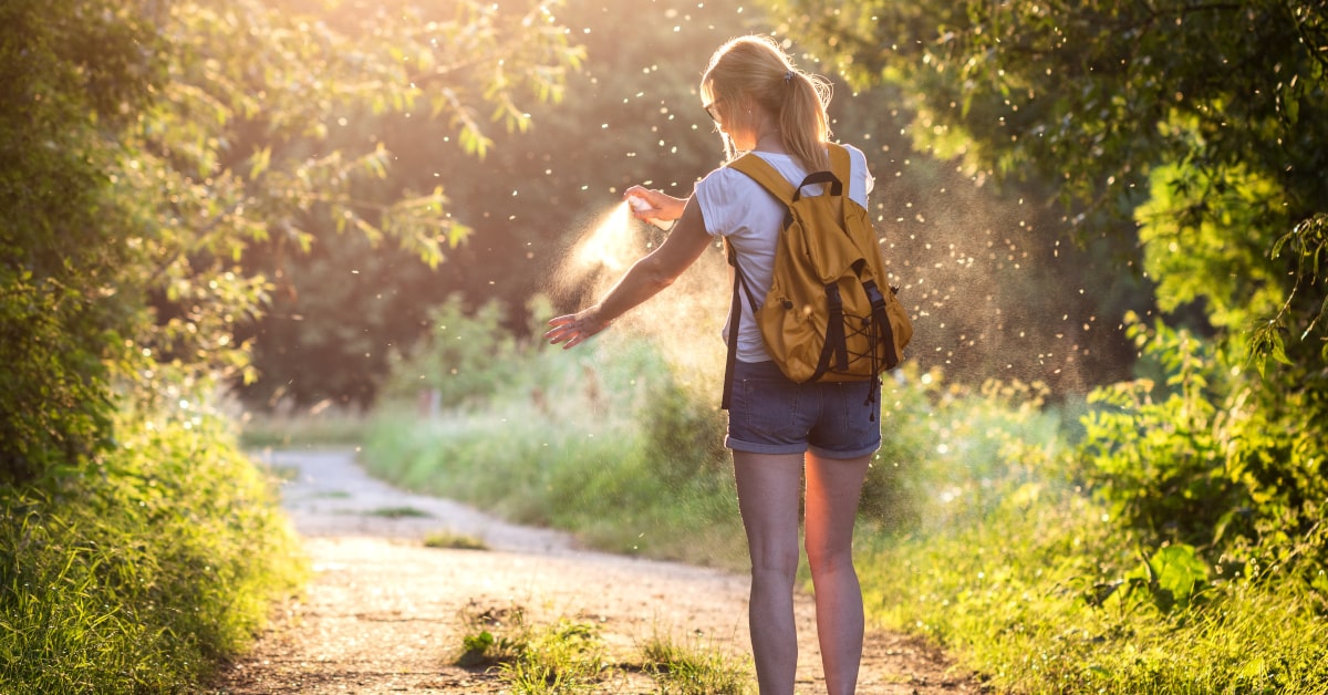 Donna in mezzo alla natura in estate che usa uno repellente per insetti