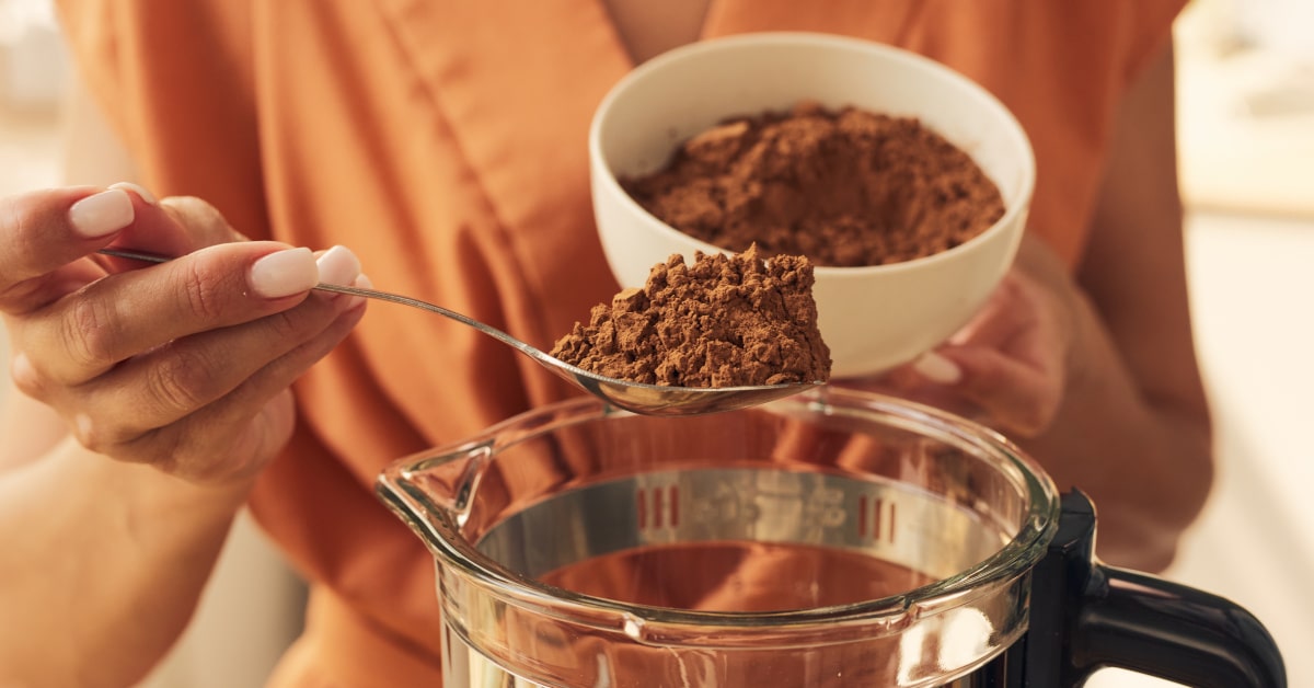 Donna che versa cacao in polvere in un frullatore 