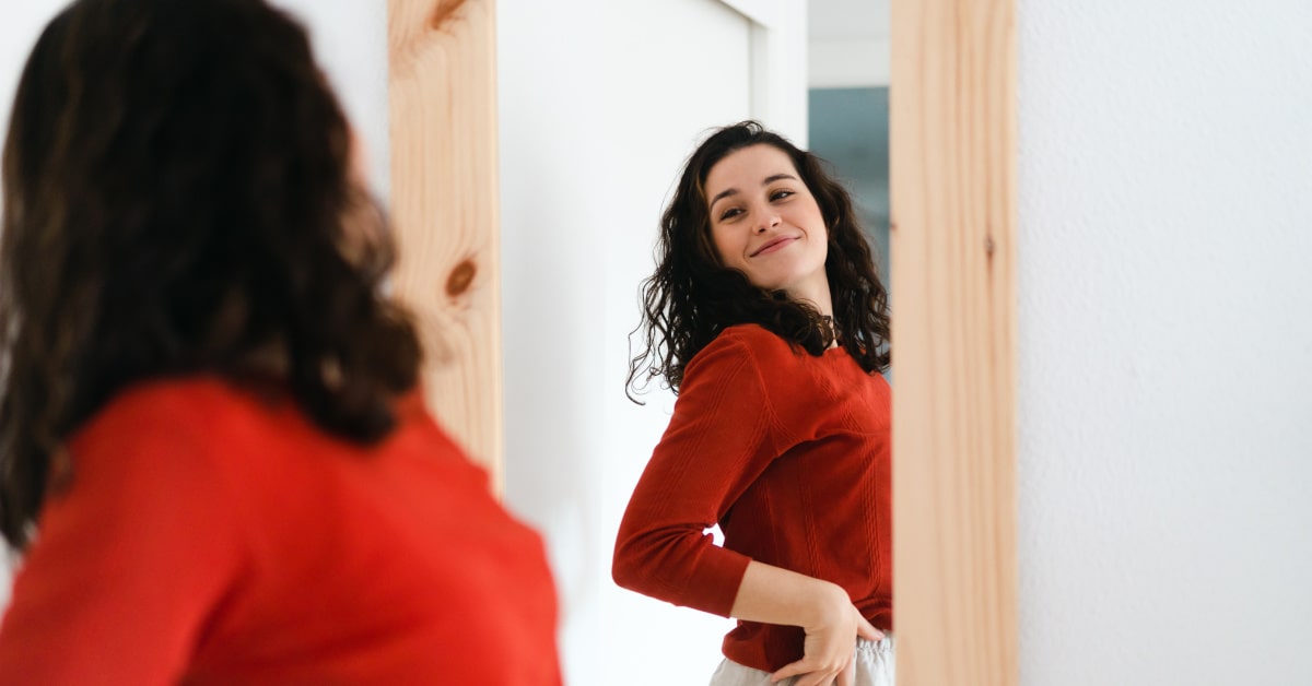 Donna con maglione rosso che si ammira allo specchio soddisfatta
