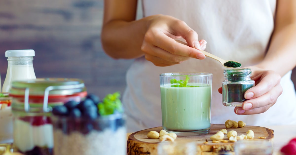 Donna che prepara un frullato vegetale con polvere di spirulina