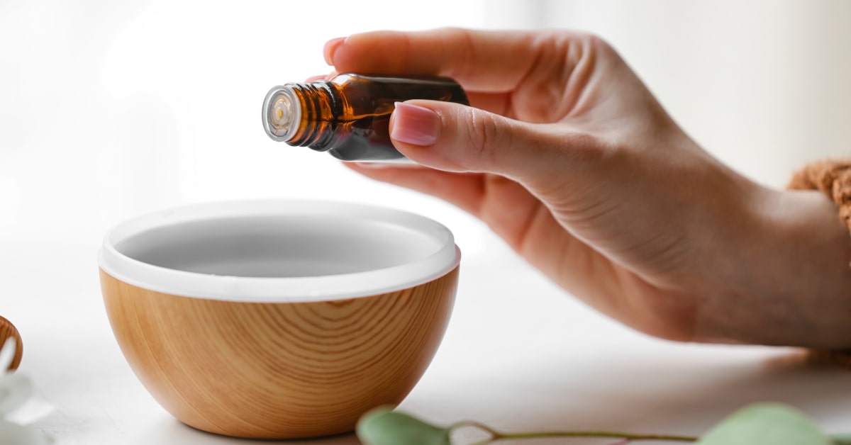 Donna che aggiunge gocce di olio essenziale nel serbatoio di un diffusore di oli essenziali