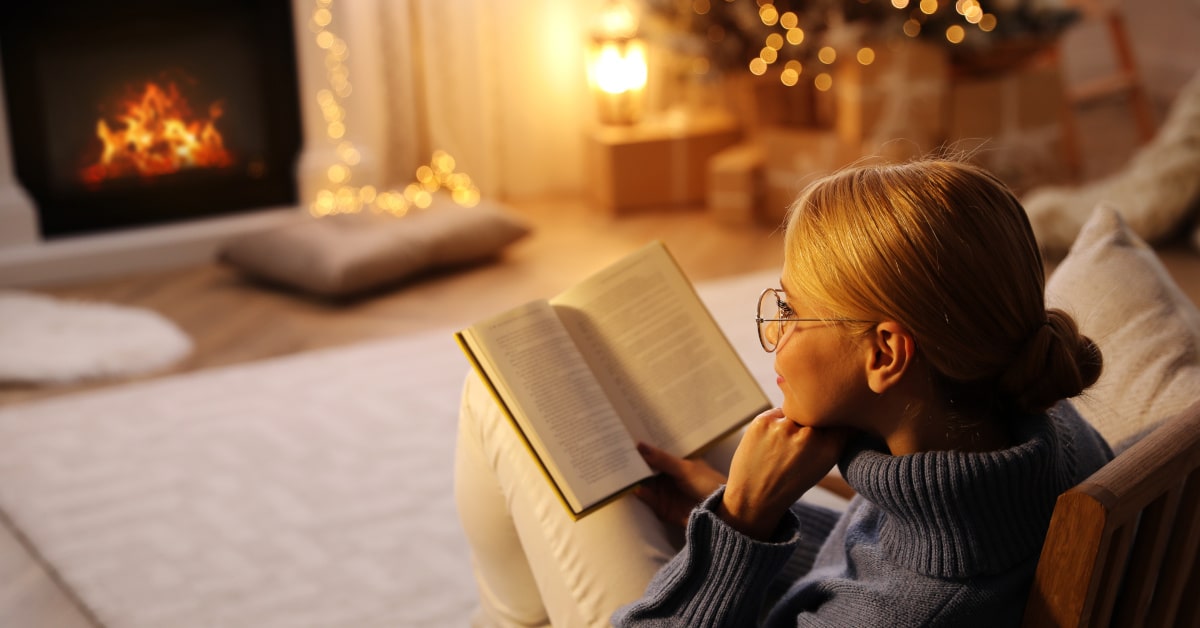 Donna che legge sulla poltrona davanti al camino e all'albero di Natale