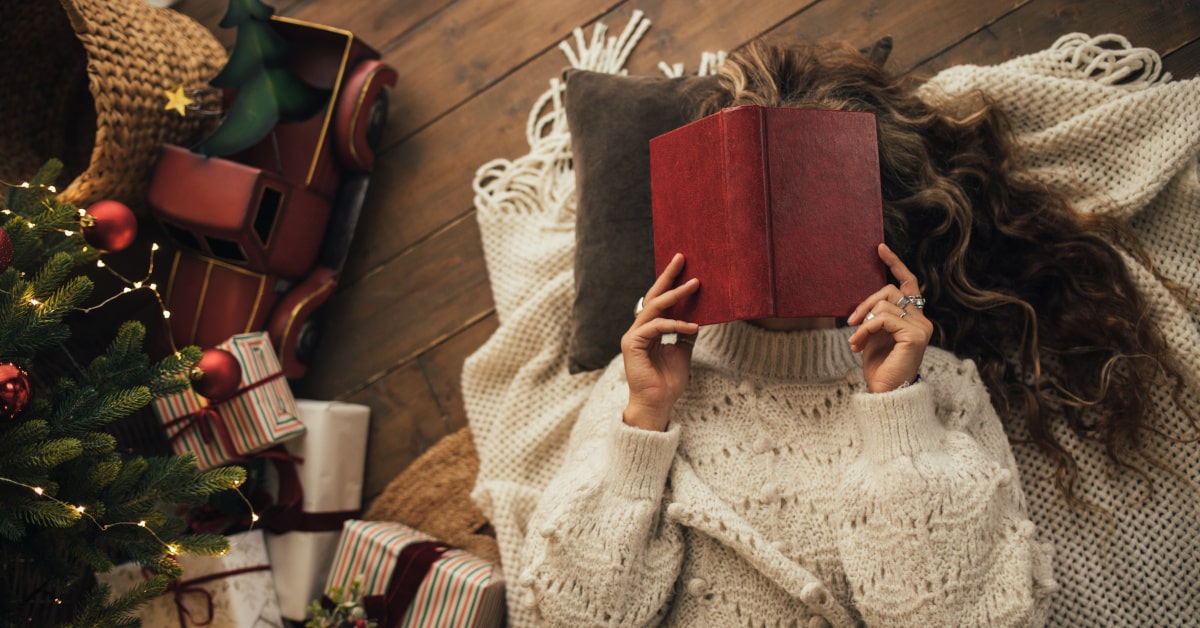 Donna stesa a terra che legge accanto all'albero di Natale