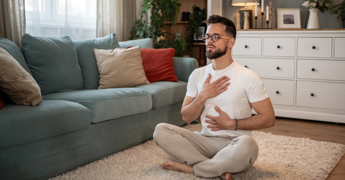 Giovane uomo seduto in salotto che fa esercizi di respirazione